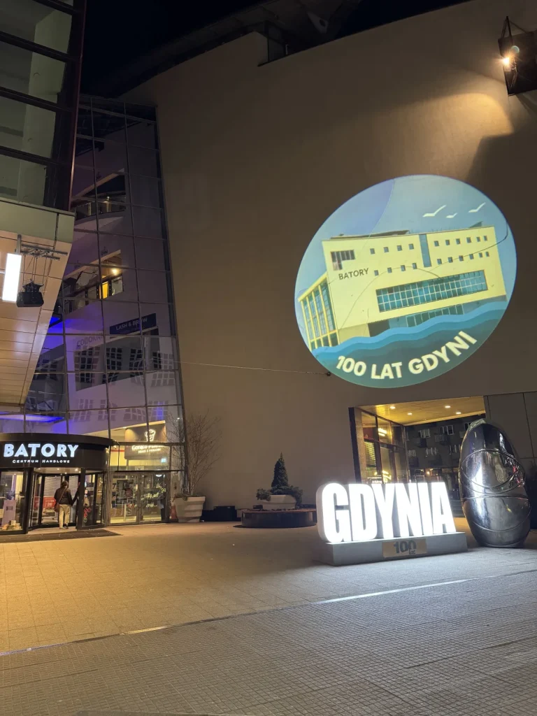 Grafika 100-lecia Gdyni wyświetlona projektorem GOBO na elewacji Galerii Batory