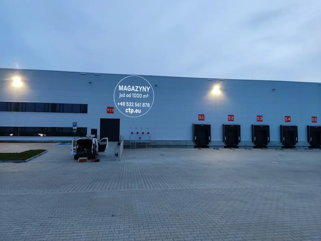 Reklama wynajmu magazynów wyświetlona na elewacji hali CTP o zmierzchu