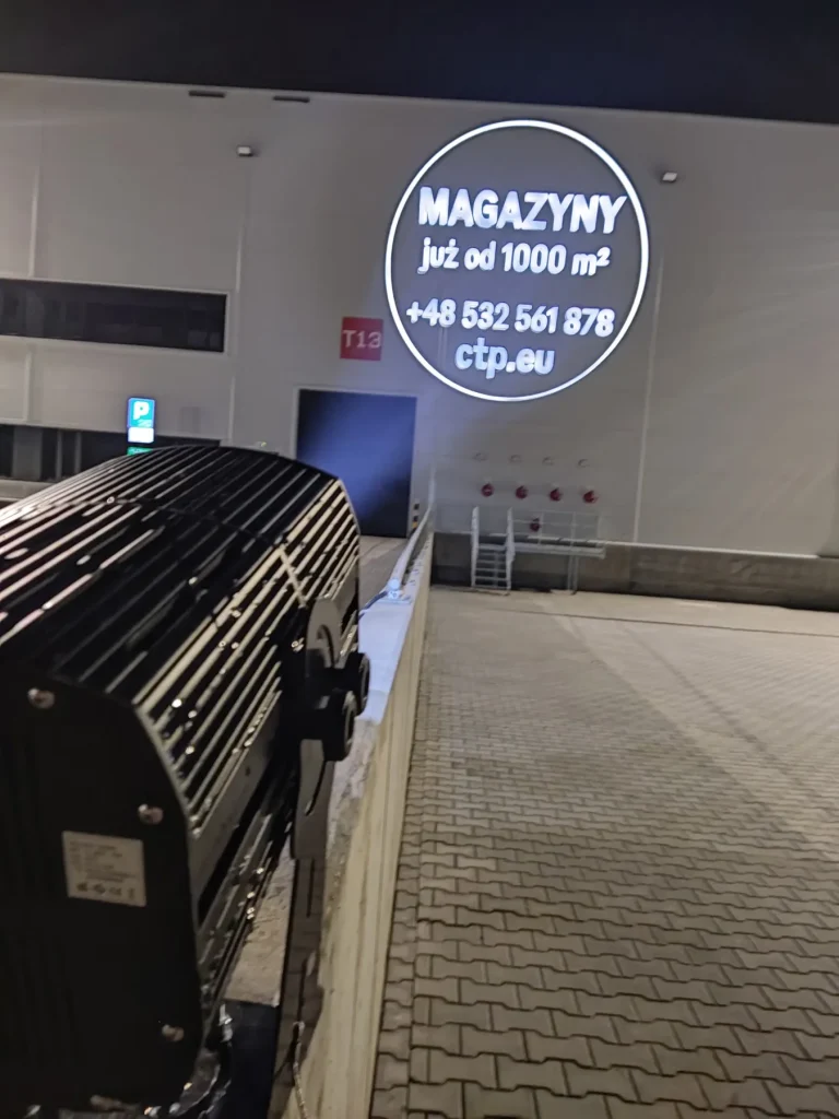Okrągła projekcja z ofertą wynajmu powierzchni magazynowej na ścianie hali