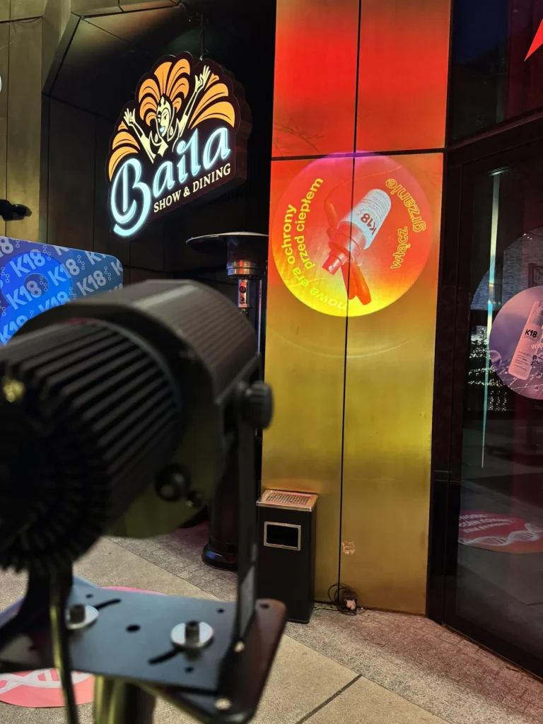 Świetlne logo wyświetlone projektorem GOBO na elewacji obok grafik promocyjnych eventu