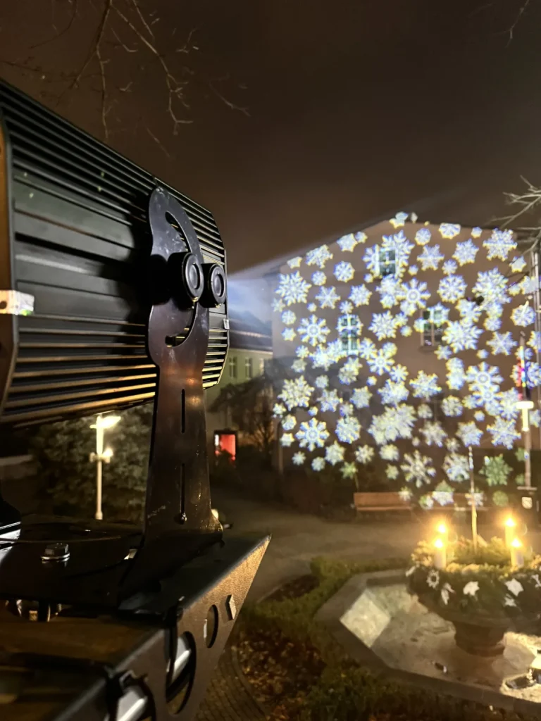 Projektor GOBO LED 600 W zamontowany na latarni i wyświetlane przez niego śnieżynki na budynku